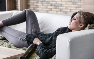 Woman passed out on a couch holding a bottle, showing potential signs of alcohol poisoning and the dangers of excessive drinking.