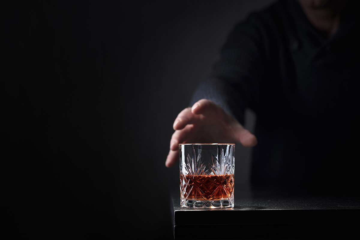 hand reaching for whiskey glass - 3 stages of alcoholism and dependence
