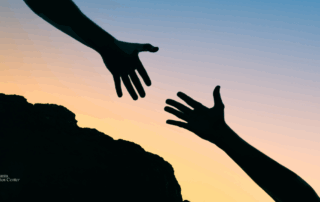 Silhouetted hands reaching out to each other against a sunset, symbolizing support, connection, and offering help to someone in need.