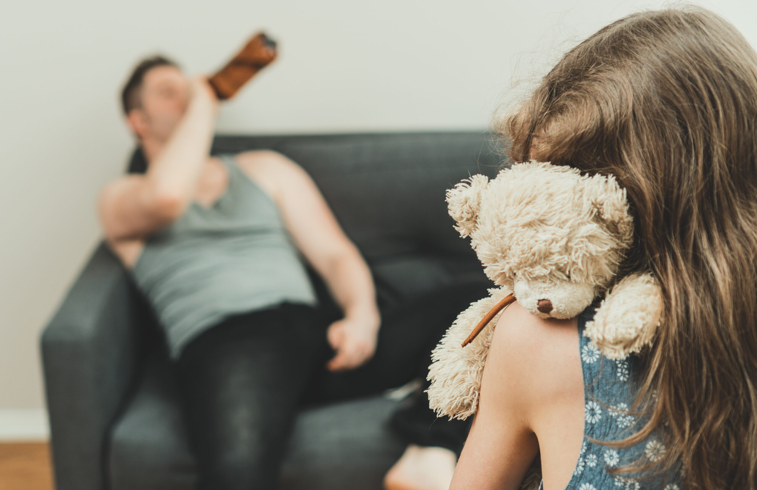 Little girl with toy standing in front of her drunk father. - Alcoholic Parent Concept image