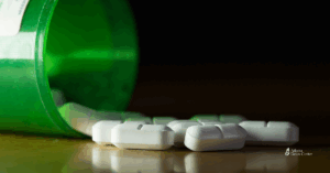 Close-up of prescription pills spilling from a green bottle onto a dark surface, symbolizing opioid misuse and the challenges of withdrawal.