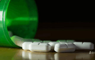 Close-up of prescription pills spilling from a green bottle onto a dark surface, symbolizing opioid misuse and the challenges of withdrawal.