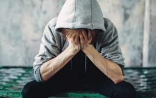 person wearing hoodie with head in hands dealing with effects of meth addiction