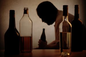 Man's silhouette behind various bottles of alcohol - About Alcohol addiction concept image