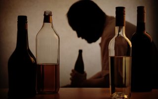 Man's silhouette behind various bottles of alcohol - About Alcohol addiction concept image