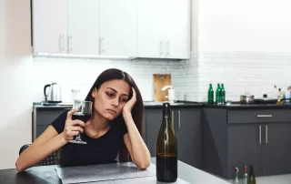 Woman drinking in a depressed state at a kitchen table - Symptoms of Alcoholism and alcohol addiction concept image