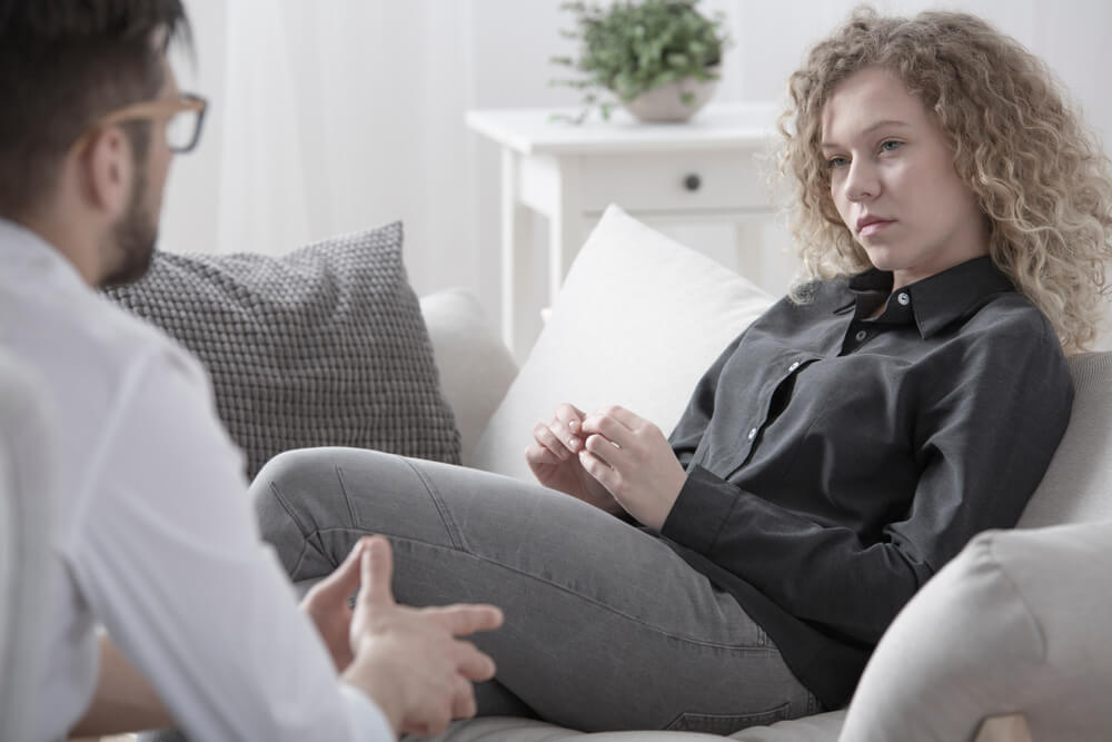 A blonde woman sits and listens to a male therapist.