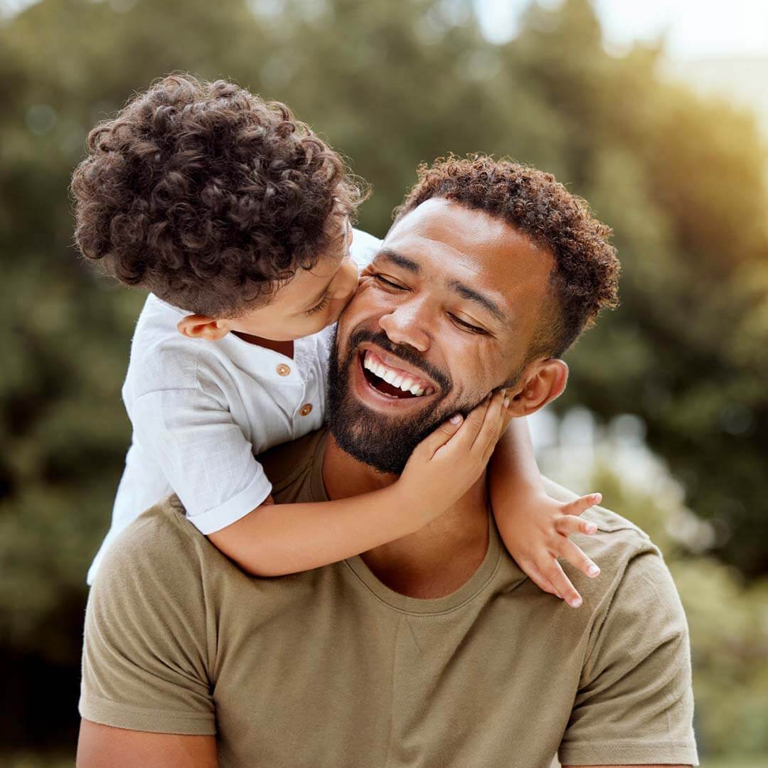 A young boy kisses his smiling father on the cheek.