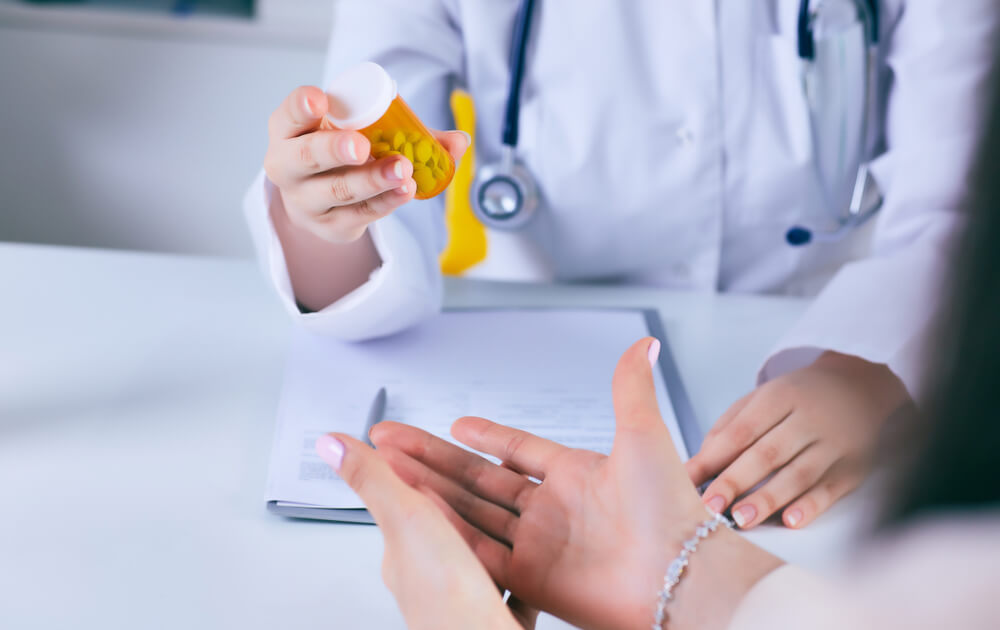 Hands of a doctor handing their patient a bottle of pills.