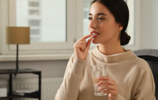 Young woman with glass of water taking dietary supplement pill indoors, space for text