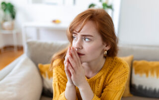 Red haired woman holds prayer hands to her lips, with a concerned expression on her face.