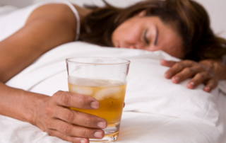 A woman lays asleep in bed with a glass full of an amber liquid.