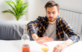 A man at a table pushes away a glass and a bottle of alcohol.