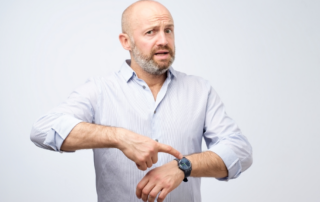 Man points at his watch with an inquisitive look on his face.