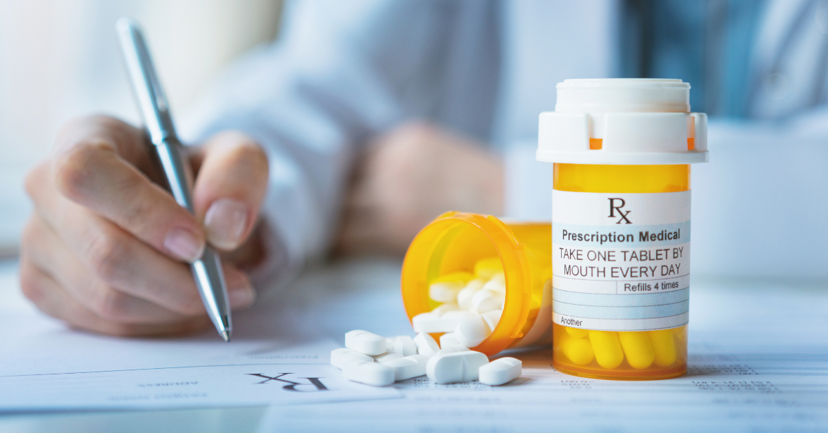 A doctor writing a script with a bottle of pills in front of them.