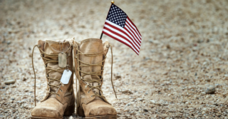 A pair of worn military boots with a dog tag and a small American flag resting on a dirt road.