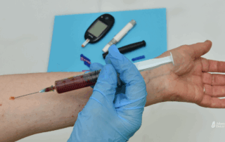 Gloved hand injecting into an arm with blood-filled syringe, surrounded by diabetic tools, symbolizing intravenous drug use and health risks linked to crystal meth dependence.