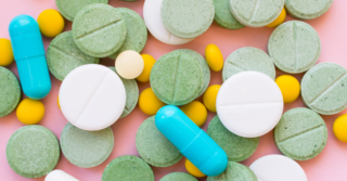 Multicolored pills, tablets and capsules against a pink background.
