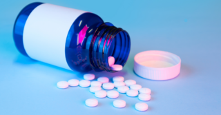 A blue pill bottle with a white label is lying on its side, spilling white round pills onto a blue surface.