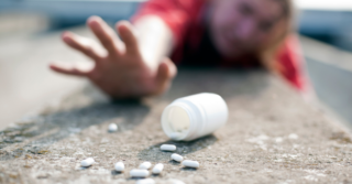 Person laying on the ground, reaching for a spilled open bottle of pills.
