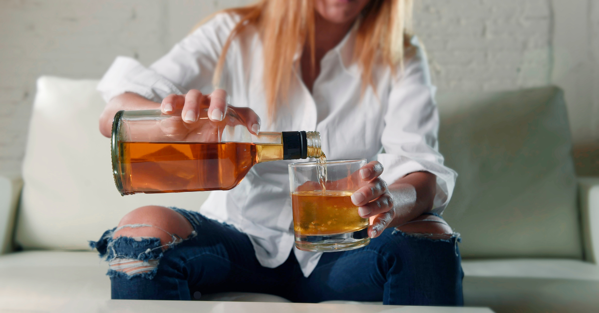 A woman pours a dark liquid from a bottle to a glass.