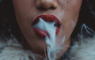 A close-up of a person's red lips as they exhale smoke, creating a dramatic and moody effect.
