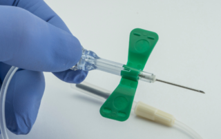 A gloved hand holding a butterfly needle, typically used for intravenous access or blood collection.