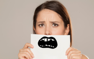 A worried woman holds a paper in front of her face with an illustration of a mouth showing damaged teeth.