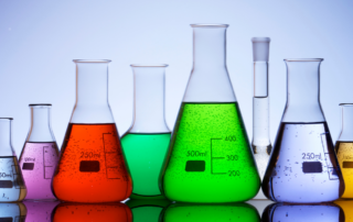 A row of laboratory flasks filled with colorful liquids, including red, green, purple, and yellow, arranged in varying sizes.