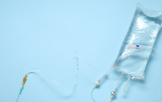 An IV bag and needle against a light blue background.