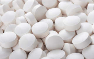 A close-up of a pile of white, round tablets, representing medication or pills.