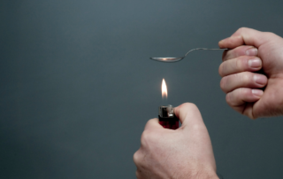 A person holding a lighter under a spoon, commonly associated with heating substances like heroin for intravenous drug use.
