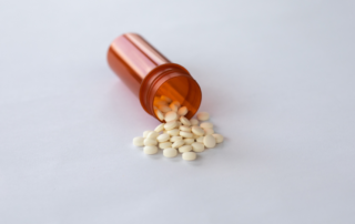 White pills spilling out of an orange pill bottle on a white surface.