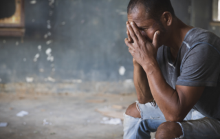 Distressed man sitting with his hands covering his face in a worn-out room, symbolizing despair or struggle.