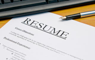 Closeup of a resume, under a pen and keyboard.