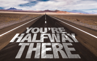 Road stretching into the distance with bold text painted on the asphalt reading "You're halfway there," symbolizing progress and motivation.