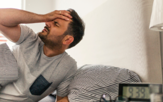 Man waking up in bed holding his head in pain.