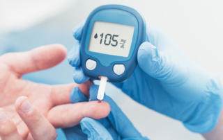 Gloved hands using a blood glucose monitor to check sugar levels, showing a reading of 105 mg/dL.