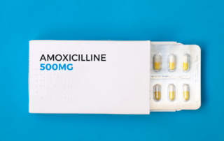 Box of Amoxicillin 500mg with blister pack of yellow and white capsules partially exposed against a blue background.