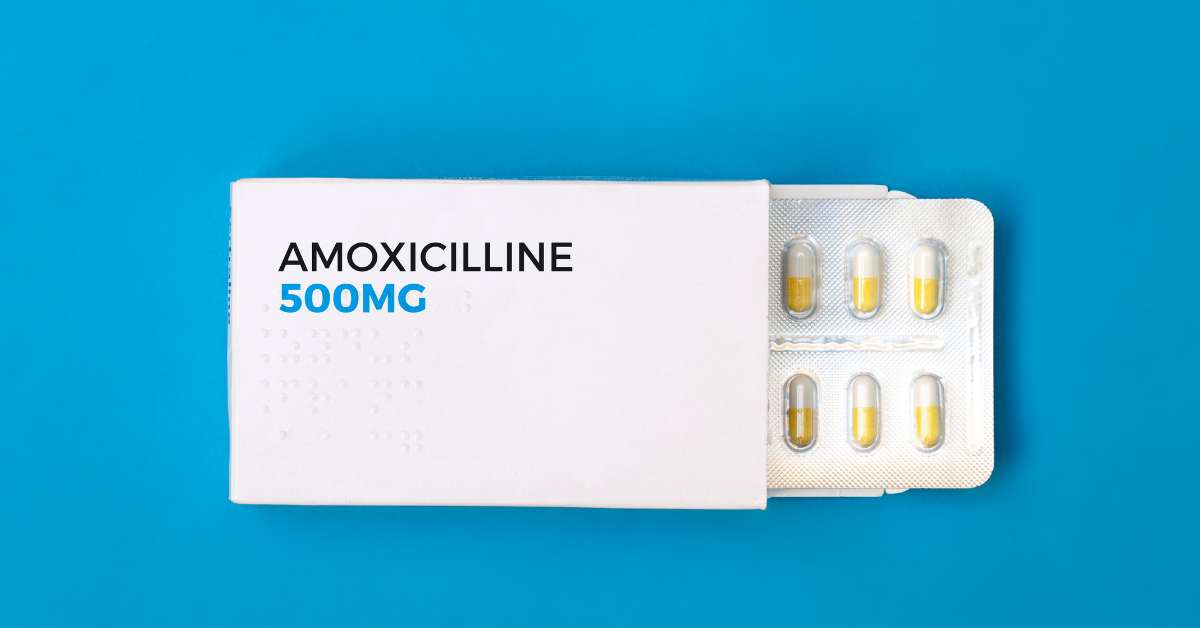 Box of Amoxicillin 500mg with blister pack of yellow and white capsules partially exposed against a blue background.