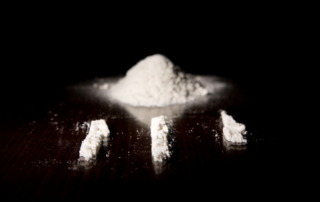 A dark background highlighting a pile of white powder and several lines of the substance arranged on a reflective surface.