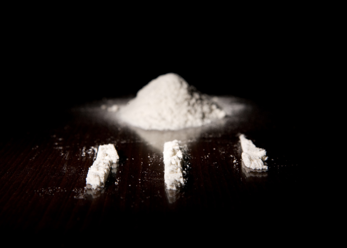 A dark background highlighting a pile of white powder and several lines of the substance arranged on a reflective surface.