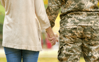 Military service member and civilian partner holding hands outdoors, symbolizing support, love, and appreciation for military spouses.
