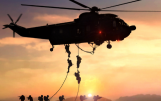 Silhouetted soldiers rappelling from a military helicopter during sunset, symbolizing the intensity and challenges of active duty service.