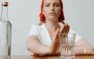 Woman holding up her hand in a refusal gesture toward a glass of alcohol, symbolizing strength and personal choice in maintaining sobriety.